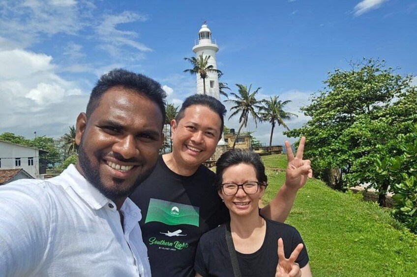 Three people taking a selfie with a lighthouse and palm trees in the background. 1