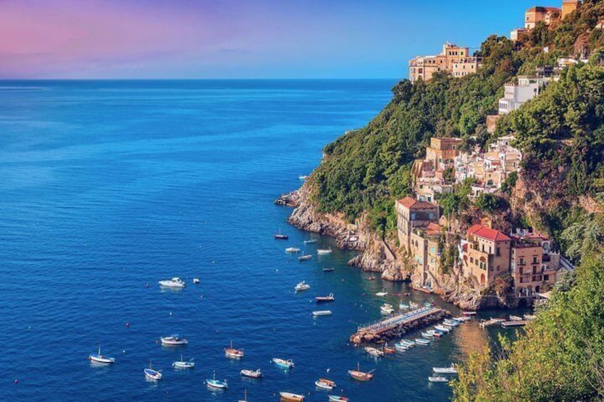 A coastal town with buildings on a hillside overlooking the sea, boats anchored near the shore, and a clear sky. 4