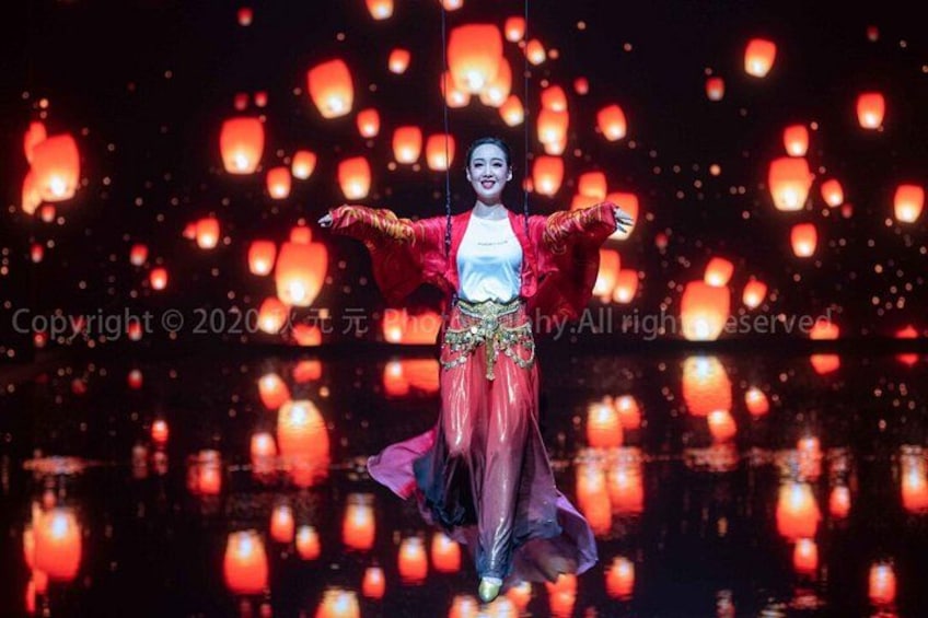 A person in traditional attire with a red and gold outfit, standing with arms outstretched against a backdrop of floating lanterns. 3