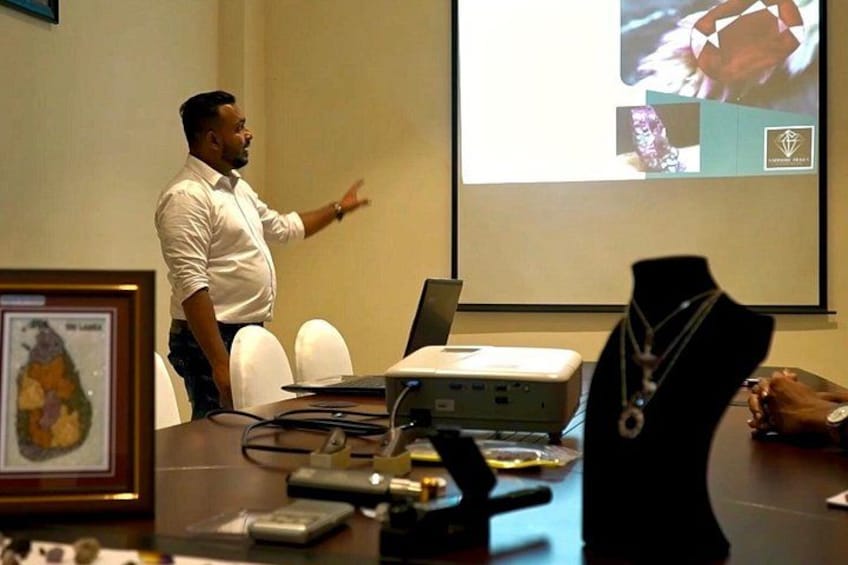 A person presenting in front of a projector screen, a laptop, and a projector on a table. 5