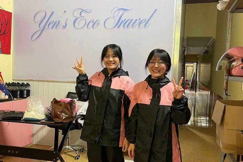 Two people in black and pink jackets posing in front of a sign that reads 'Yen's Eco Travel'. 2