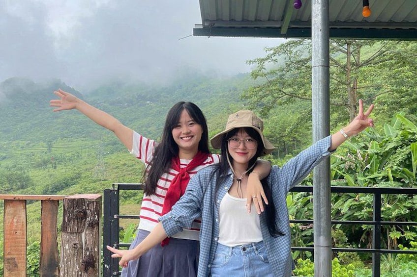 Two people standing on a wooden platform with greenery in the background. 3