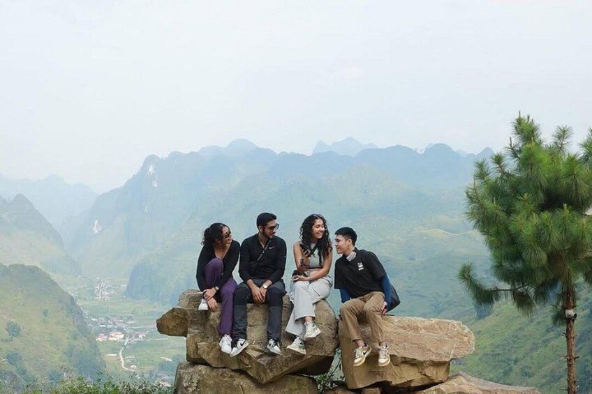 A group of people sitting on a rock formation with a mountainous landscape in the background. 1