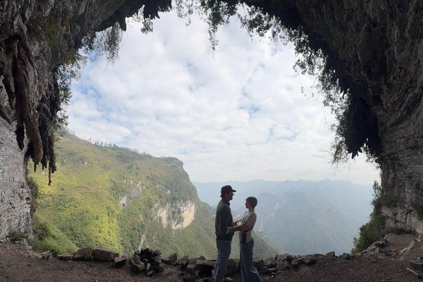 Two people standing in a cave with a view of a mountainous landscape. 5