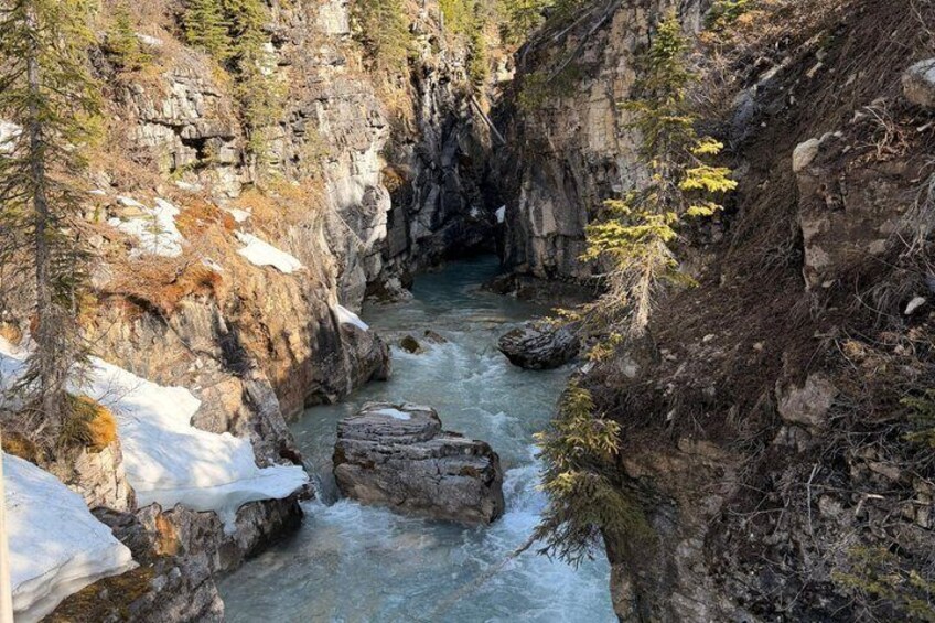 Eine Schlucht mit einem Fluss, steinernen Felswänden und Schneeflecken. 4