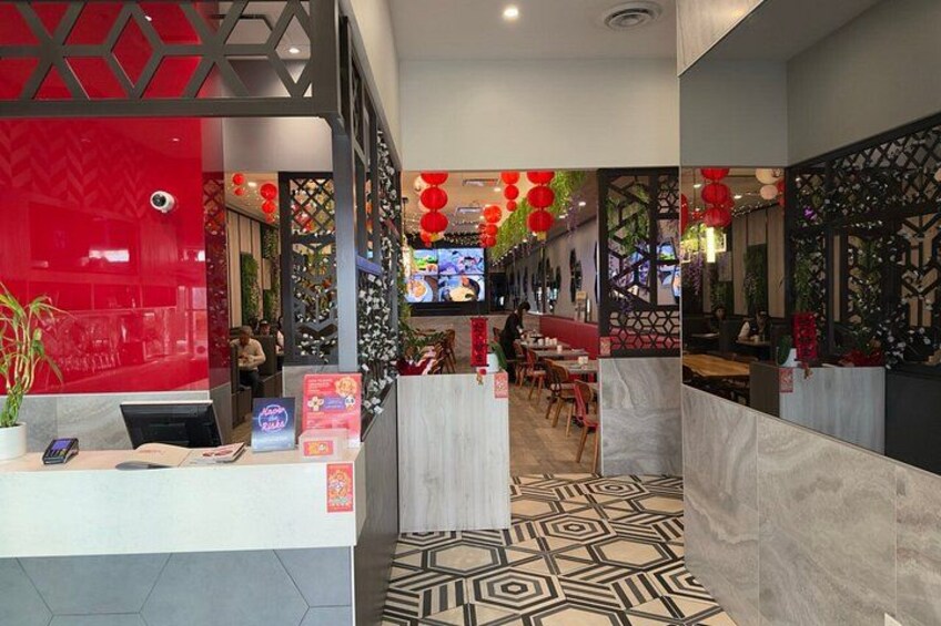 A restaurant interior with a reception desk, patterned flooring, and red decorations. 3