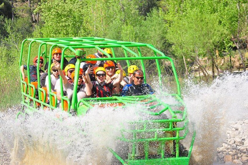 A group of people in a green raft navigating through a river with water splashing around. 1