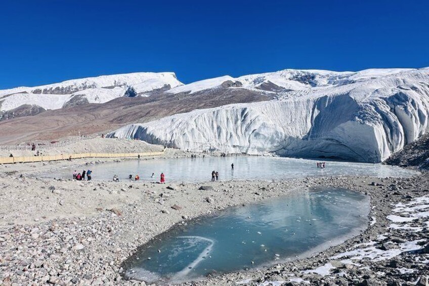 Un glaciar con un pequeño lago al frente y personas observándolo. 4