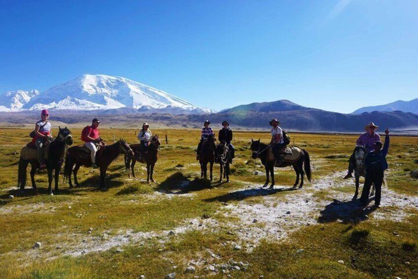 Un grupo de personas montando a caballo en un campo cubierto de hierba, con una montaña nevada al fondo. 2