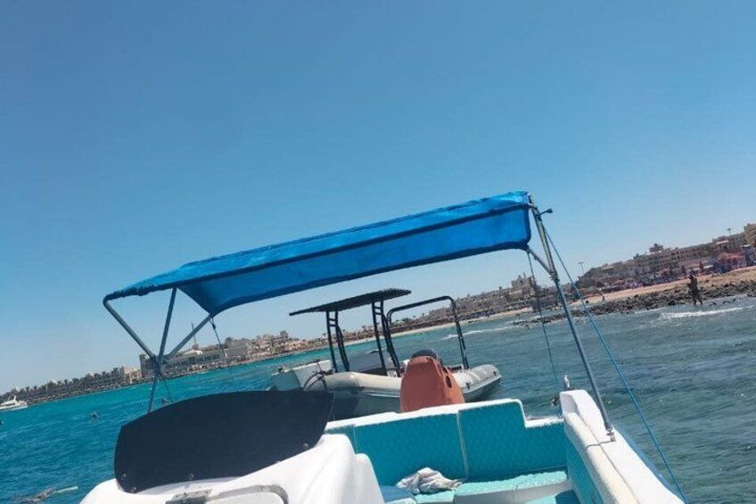 Un barco con toldo azul, mar en calma y un pueblo costero al fondo. 4