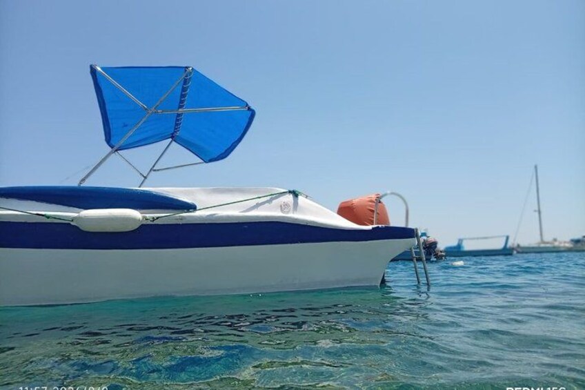 Un bote con toldo azul y una boya naranja, anclado cerca de un muelle bajo un cielo azul despejado. 5
