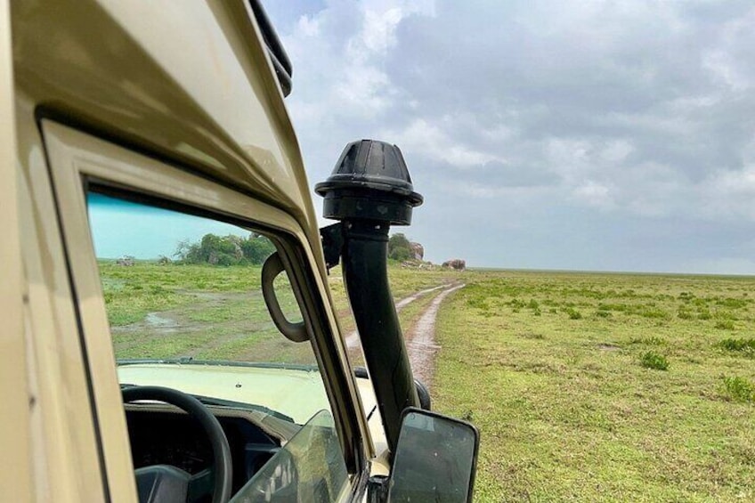 A vehicle's interior with a view of a dirt road in a grassy field. 2