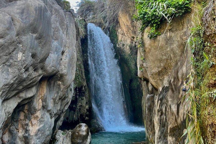A waterfall cascading down a rocky cliff surrounded by greenery. 1