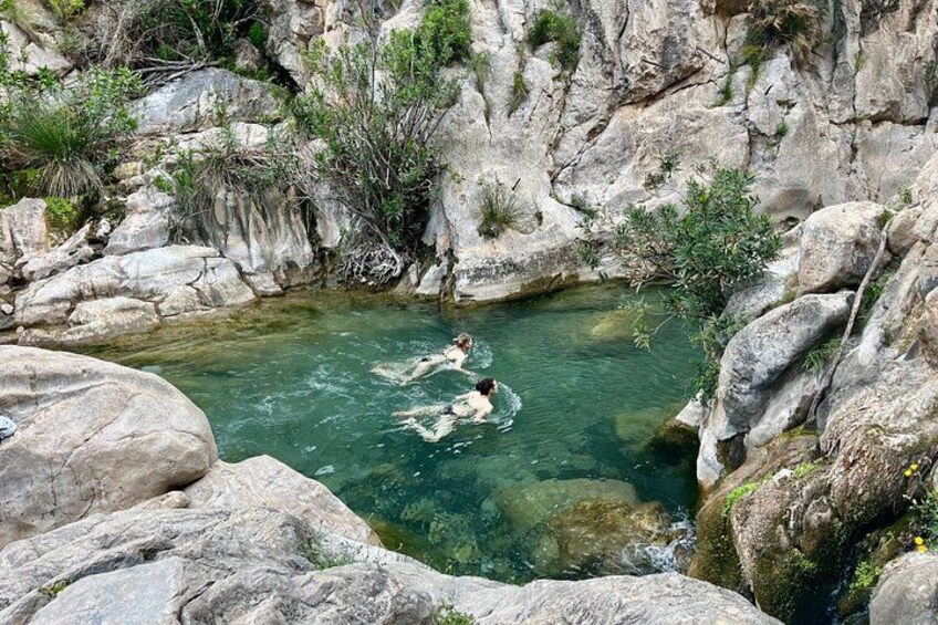 A natural pool surrounded by rocky terrain with two people swimming. 2
