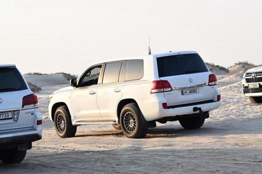 Un SUV blanco estacionado en una playa arenosa con cielo despejado. 2