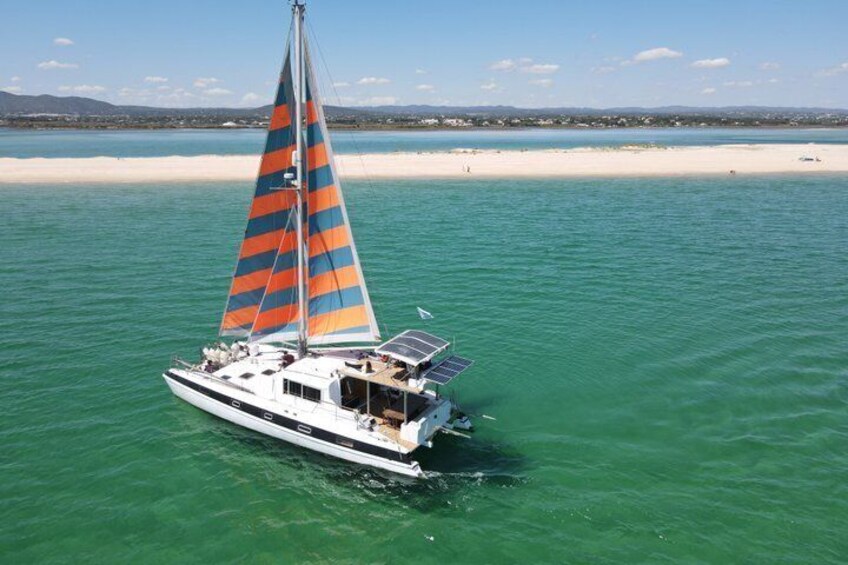 Een zeilboot met een kleurrijk zeil op turquoise water nabij een zandstrand. 1