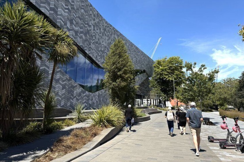 En moderne bygning med en unik geometrisk facade, omgivet af palmer og en belagt sti. 2