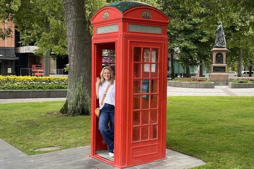A red telephone booth in a park with a statue in the background. 4