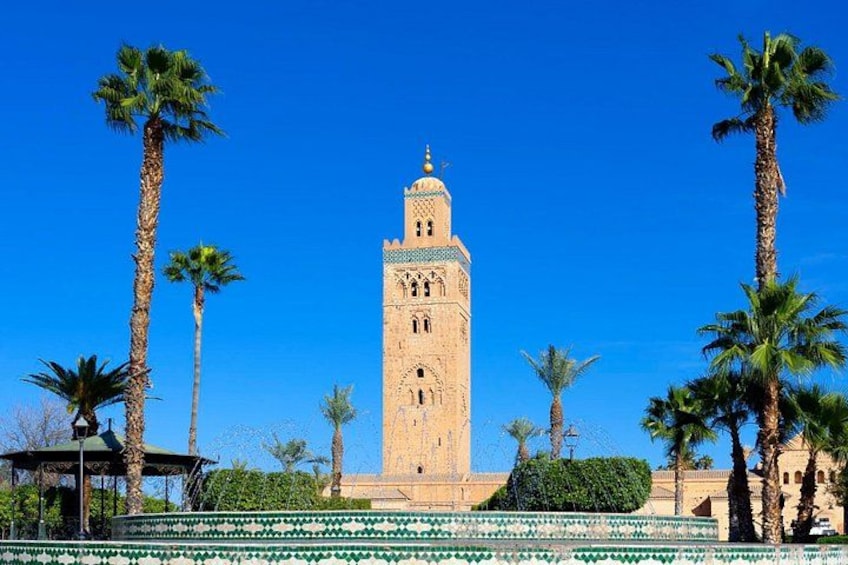 Ein hoher Turm mit einer Minarette, umgeben von Palmen und einem geometrisch angelegten Garten. 4