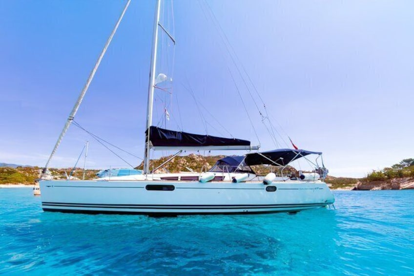 A sailboat on a clear blue sea with rocky coastline in the background. 1