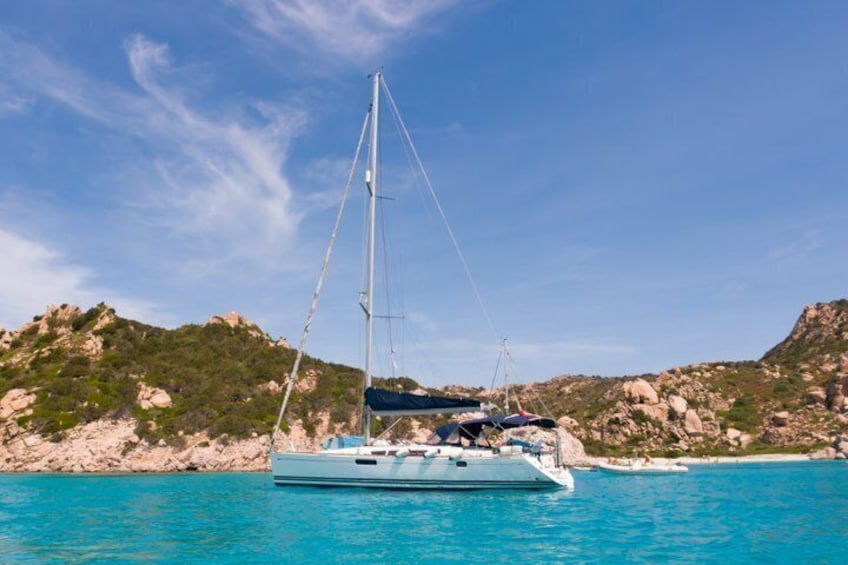 A sailboat on turquoise water with rocky hills in the background. 3