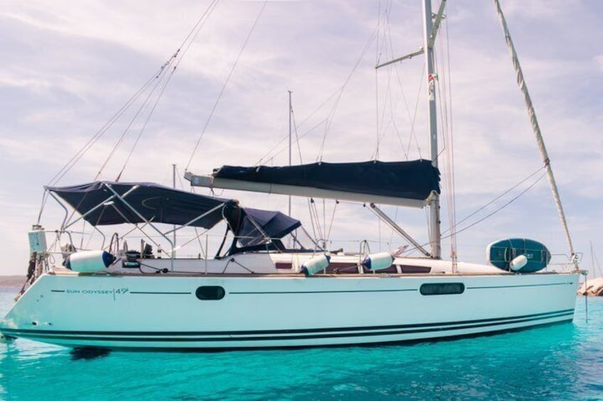 A sailboat named 'Sun Odyssey 149' with a light blue hull, sails, and a canopy on the deck. 2