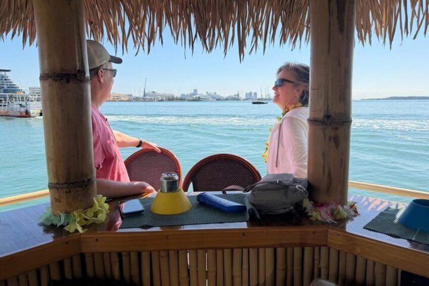 A couple dining at a wooden table with a view of the water and a city skyline in the background. 3
