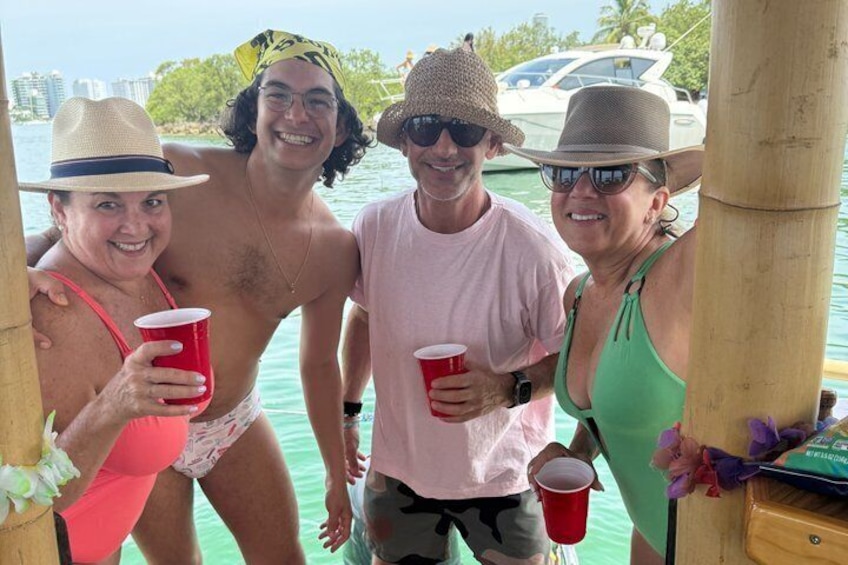 A group of people on a boat, holding red cups, with a body of water and a cityscape in the background. 5