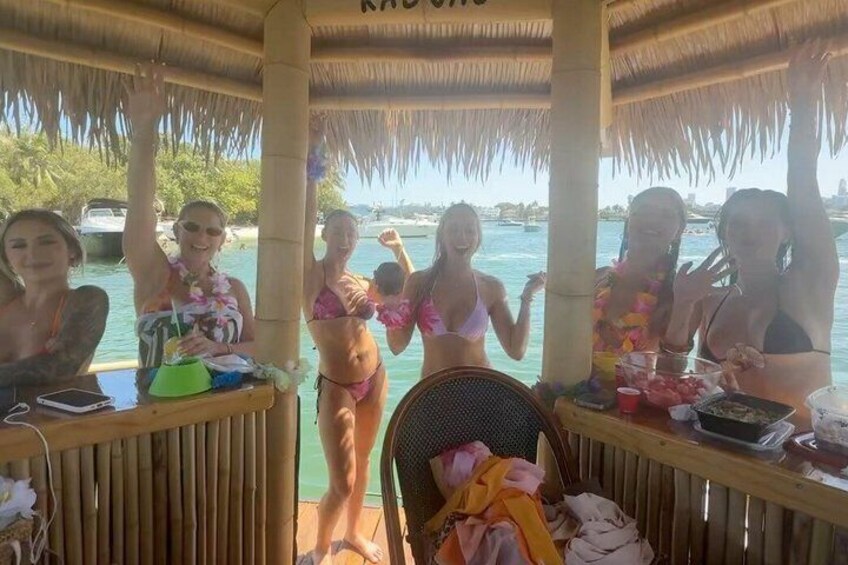 A group of people on a boat with a thatched roof, enjoying drinks and food. 1