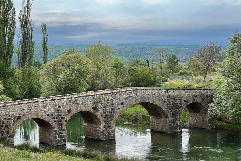 A stone bridge over a river with trees and a distant view. 4
