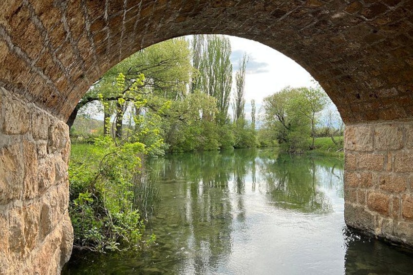 A stone bridge arching over a calm river, surrounded by lush greenery and trees. 3