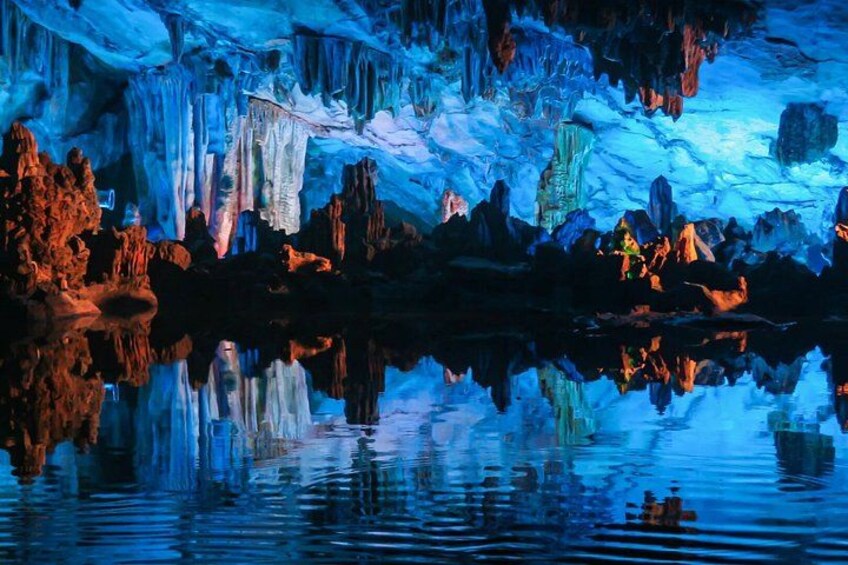 A cave with stalactites and stalagmites, illuminated by blue lighting, reflecting on the water surface. 2