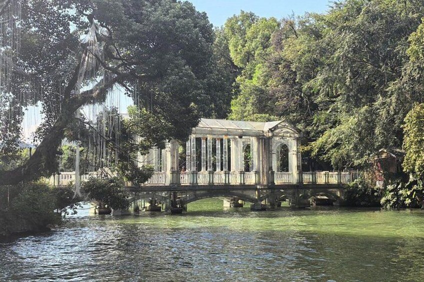 A gazebo on a bridge over a pond, surrounded by trees and greenery. 4