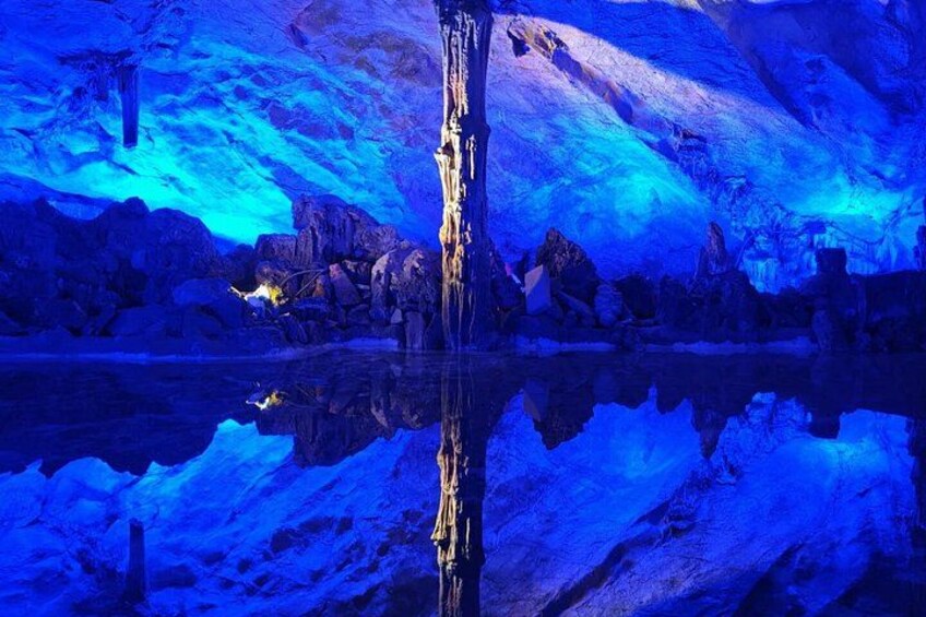A cave with blue lighting, a reflective water surface, and rock formations. 3