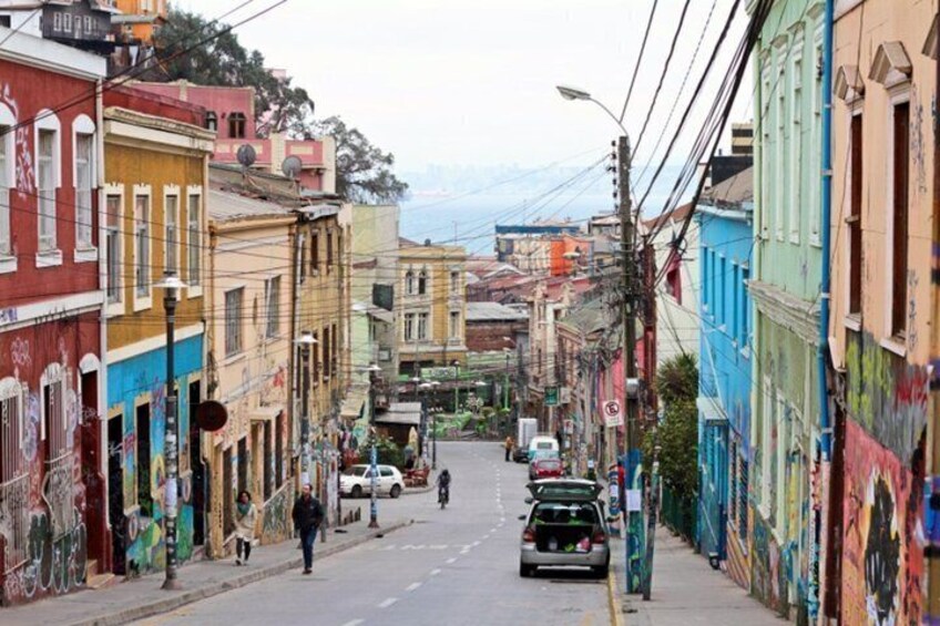 A narrow street lined with colorful buildings, a few pedestrians, and parked cars. 2