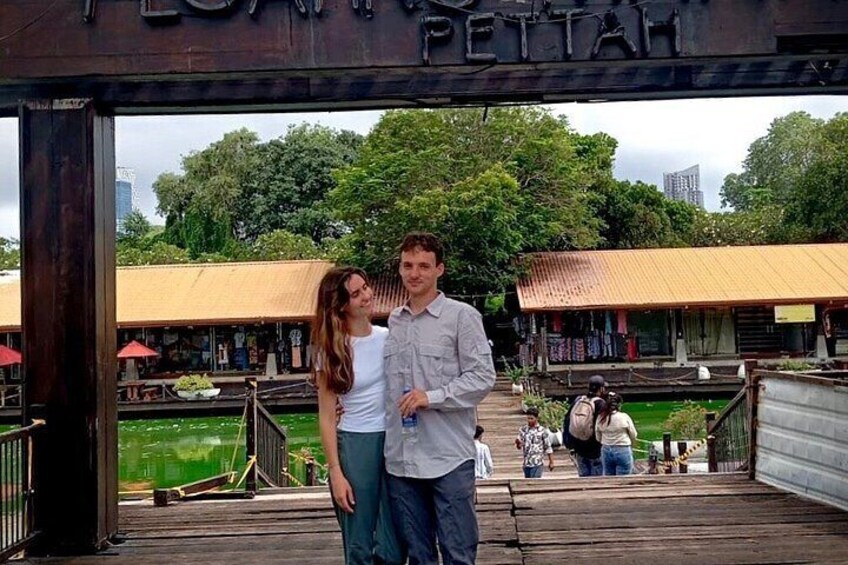 A wooden bridge with a sign reading 'Pettah' and a view of a water body and buildings in the background. 3