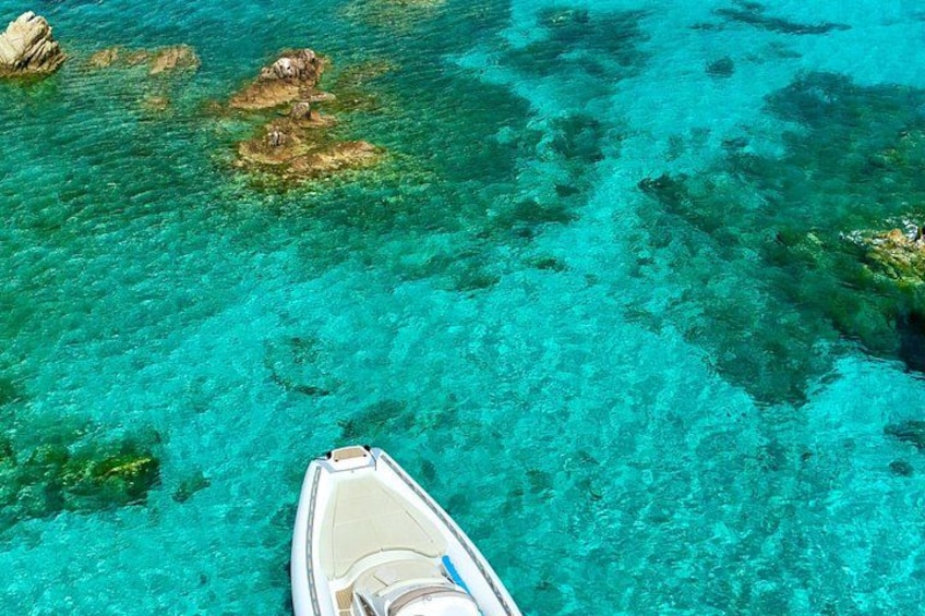 A boat on clear turquoise water with visible rocks and coral formations. 3