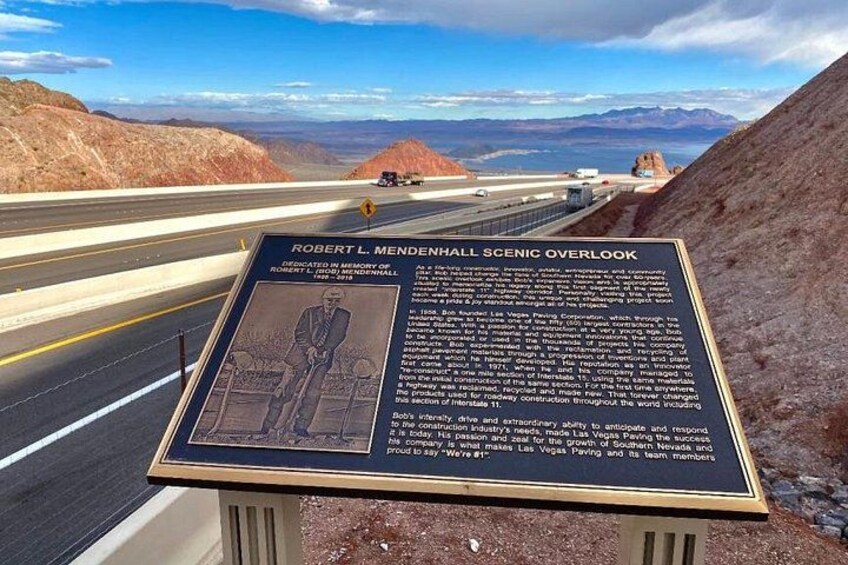 A scenic overlook sign with a view of a highway and mountains. 4