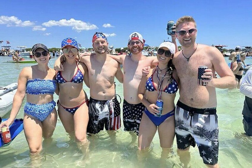 Eine Gruppe von Personen in Badekleidung an einem Strand mit klarem Wasser und einem Boot im Hintergrund. 3