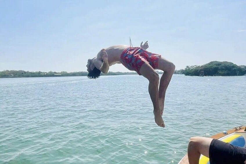 Eine Person schwebt in der Luft über dem Wasser, trägt Badesachen, im Hintergrund ein Boot und eine kleine Insel. 4