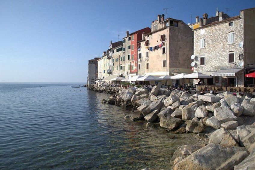 A coastal town with stone buildings, a rocky shoreline, and clear blue water. 3