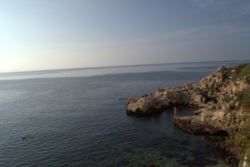 A coastal landscape with clear water, rocky cliffs, and a distant shoreline. 5