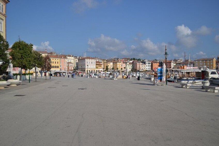 A wide open square with buildings in the background and boats docked along the waterfront. 4