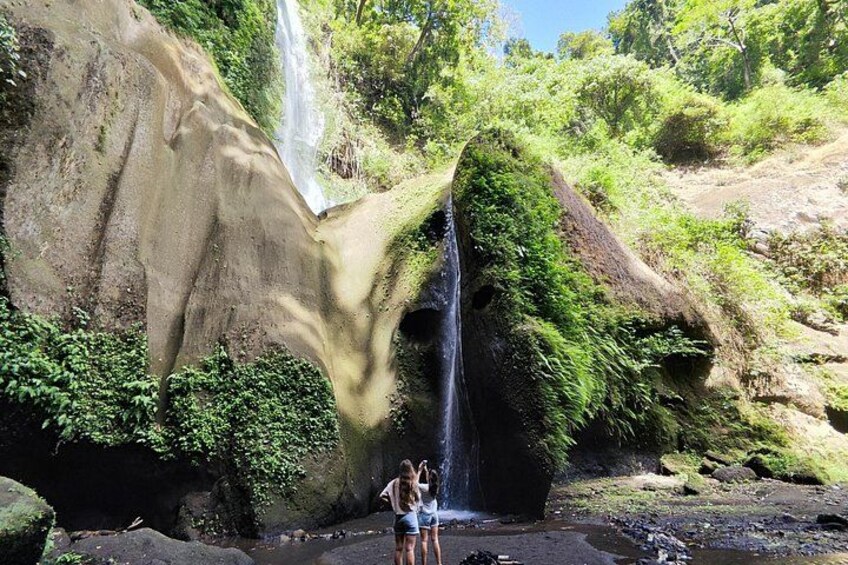 A waterfall cascading down a rocky cliff surrounded by lush greenery. 2