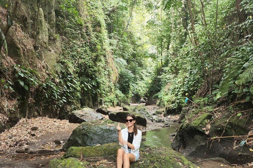 A person sitting on a rock by a stream in a forested area. 4