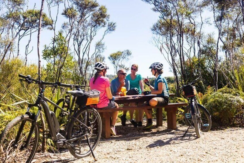A group of people sitting at a wooden table outdoors with bicycles parked nearby. 3