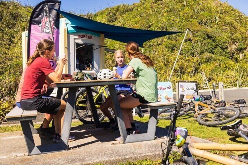 Three people sitting at a table under a tent with a coffee stand in the background. 2
