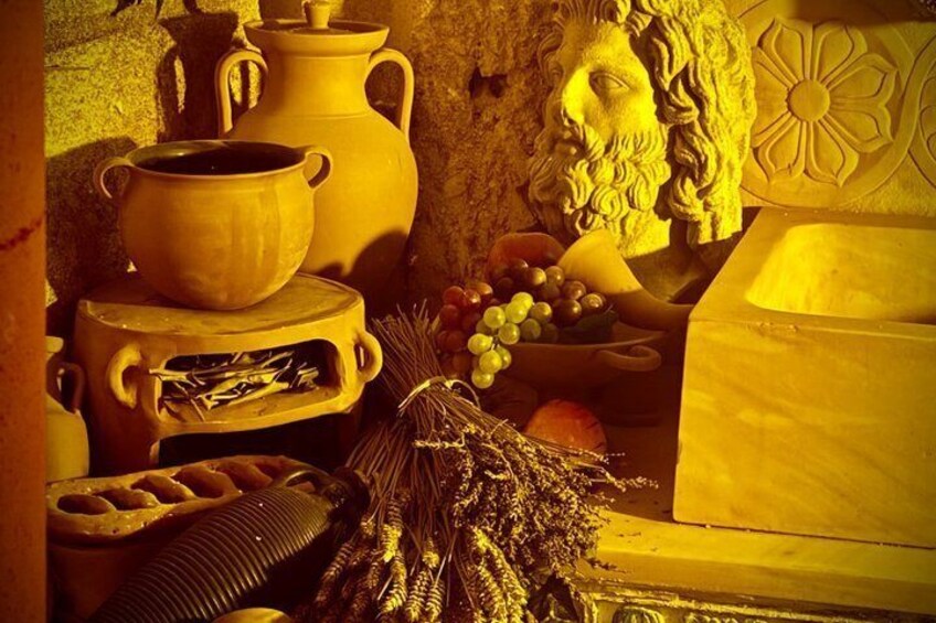 A rustic kitchen setting with pottery, a statue, and fresh produce. 3
