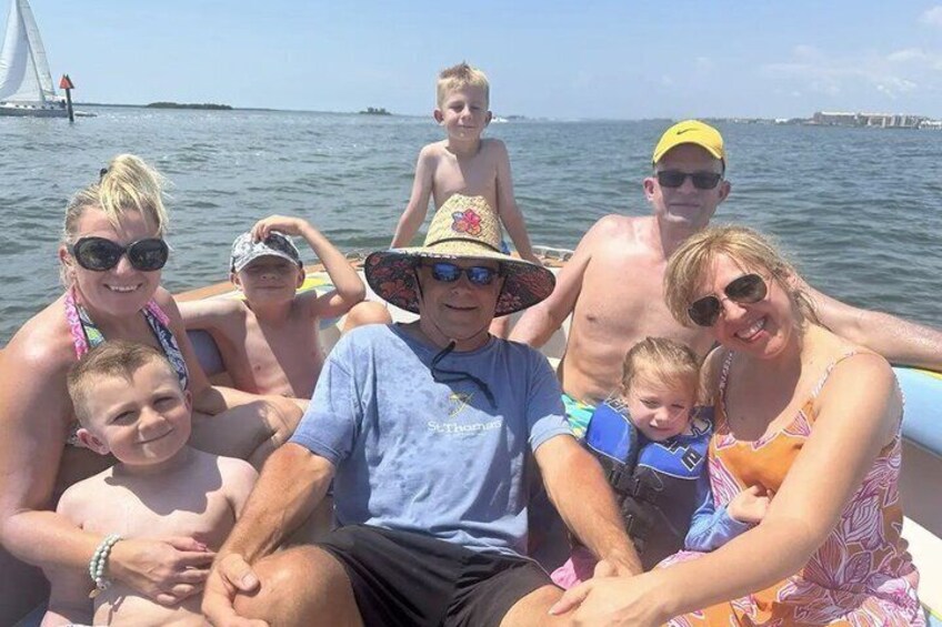 Une famille à bord d’un bateau, avec un voilier en arrière-plan. 5