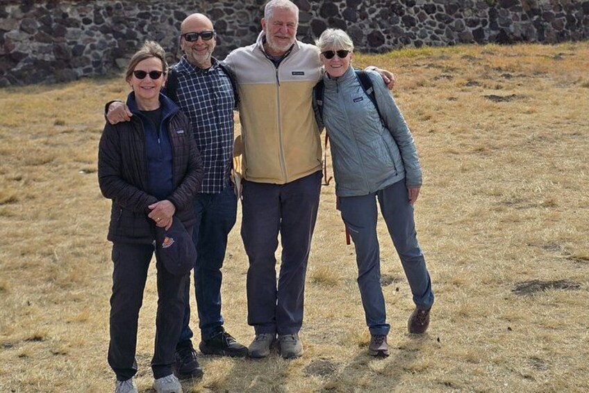 Quattro persone in piedi su un prato, con un muro di pietra sullo sfondo. 2